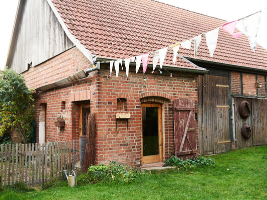 English: Traditional brick workshop with wooden barn doors and bunting in a German countryside garden / ドイツの庭にあるレンガ造りの工房と木製の納屋扉、旗が飾られた風景