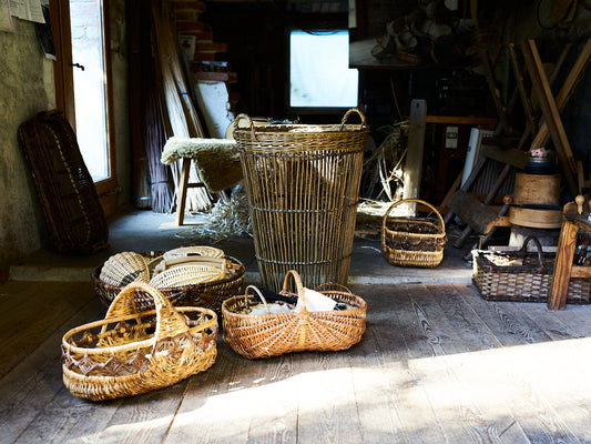 Various handmade baskets arranged on a wooden floor inside a German workshop with soft natural light / ドイツの工房内、やわらかな自然光の中で木の床に並ぶ手編みのかごたち