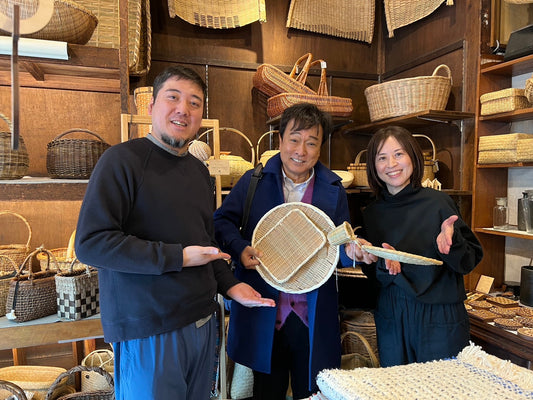Television guest holding a purchased bamboo sieve with the shop owner couple inside a basket store / テレビ番組「ぶらり途中下車の旅」取材にて、購入した竹ざるを手にした来店者と、両脇に立つ市川籠店の店主夫妻