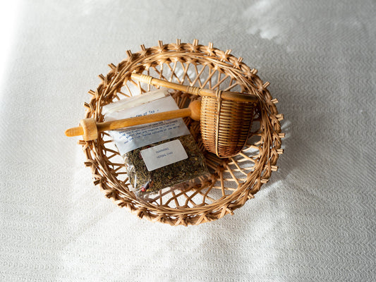 Willow basket with herbal tea and a tea strainer placed on fabric / 布の上に置かれた、ハーブティーと茶こしの入ったやなぎのかご