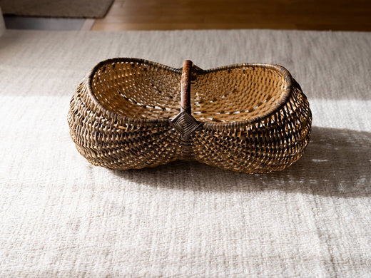 Handwoven hazel and willow basket with a central handle placed on fabric / 布の上に置かれた、中央に持ち手のあるヘーゼルとやなぎの手編みかご