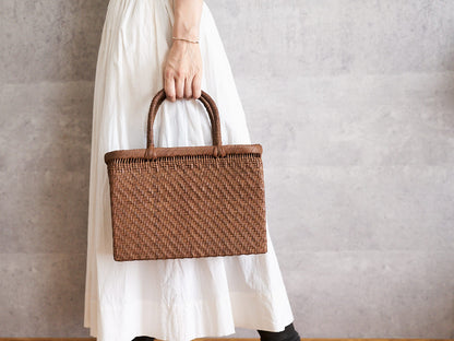 A person holding a structured grapevine basket bag by its handles / やまぶどうの四角い手提げかごを手に持っている様子