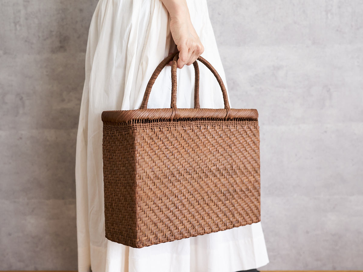 A person holding an A4 grapevine tote basket by its handles / やまぶどうのA4トートバッグを手に持っている様子