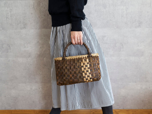 Walnut bark plump checker handbag with front light strip held in hand / くるみの裏皮市松編み手提げ（表皮ライン入り・ふっくら）を手に持った様子