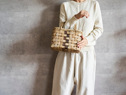 Walnut bark checker handbag with center dark strip held in hand / くるみの表皮市松編み手提げ（中央裏皮ライン）を手に持った様子