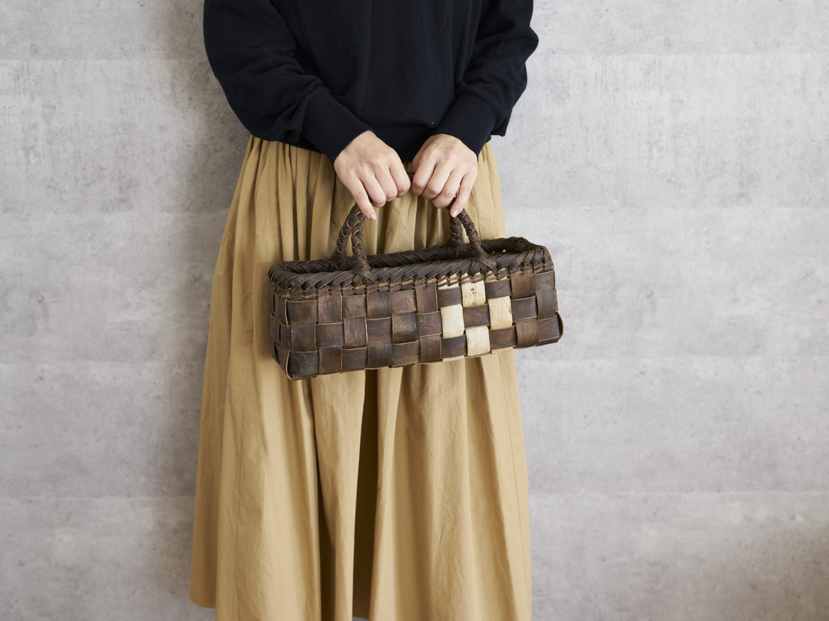 Walnut bark shallow handbag with checker weave held in hand / くるみの浅型・裏皮市松編み手提げ（表皮ライン入り）を手に持った様子