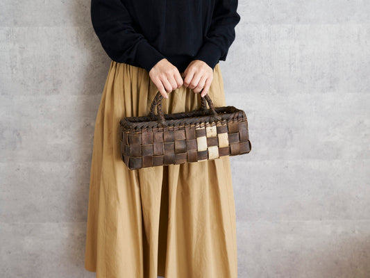 Walnut bark shallow handbag with checker weave held in hand / くるみの浅型・裏皮市松編み手提げ（表皮ライン入り）を手に持った様子