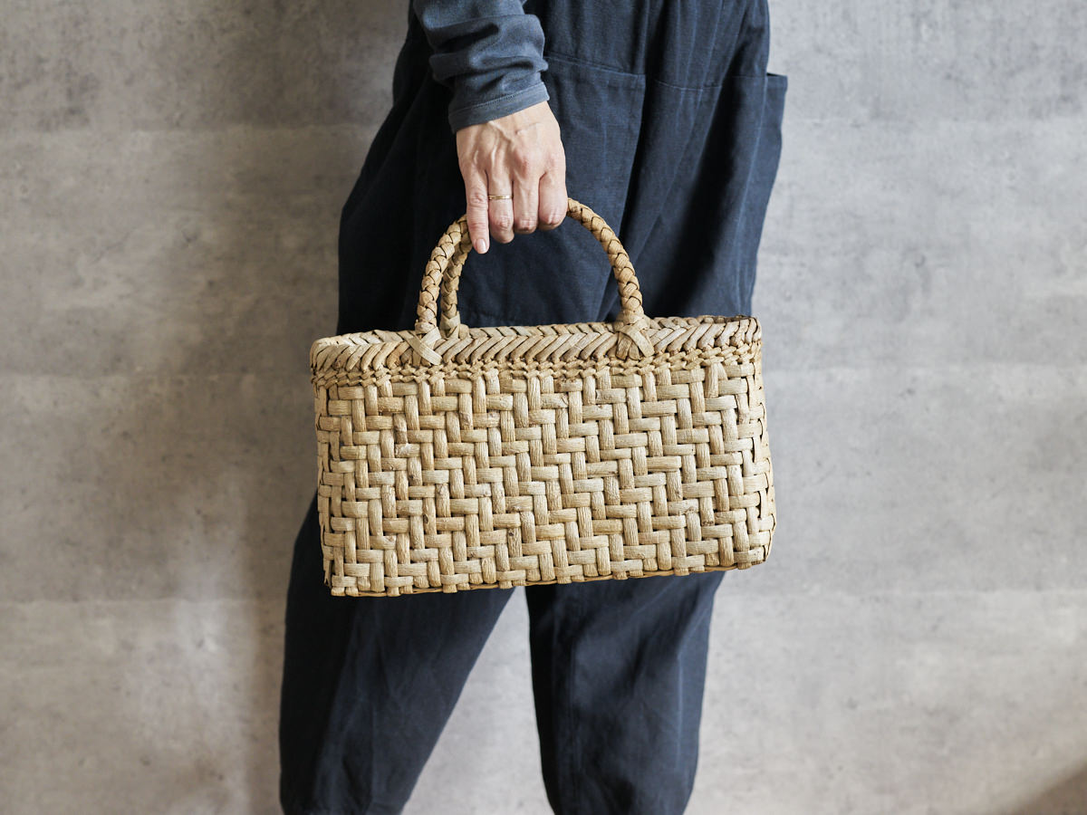 Walnut bark herringbone-weave handbag held in hand / くるみの総表皮あじろ編み手提げを手に持った様子
