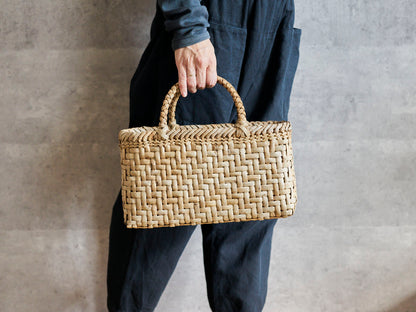 Walnut bark herringbone-weave handbag held in hand / くるみの総表皮あじろ編み手提げを手に持った様子