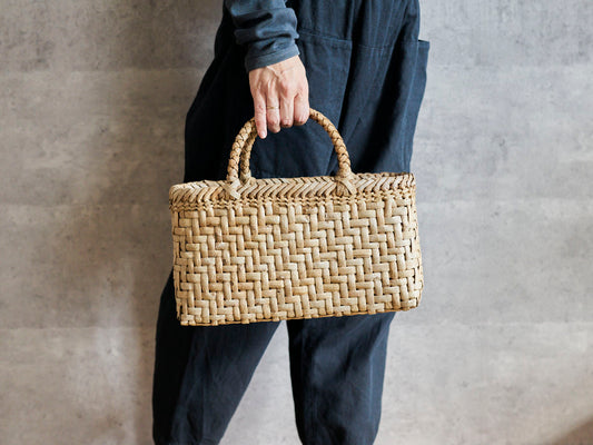 Walnut bark herringbone-weave handbag held in hand / くるみの総表皮あじろ編み手提げを手に持った様子