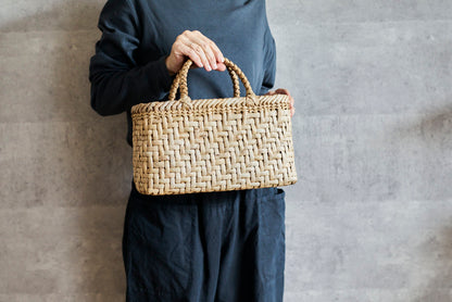Walnut bark herringbone-weave handbag held in hand / くるみの総表皮あじろ編み手提げを手に持った様子