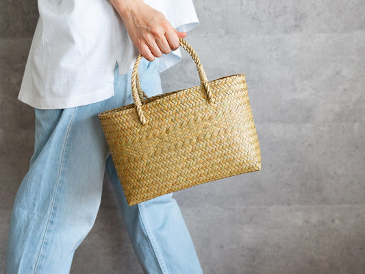 Hand holding a slim oval Krajood grass basket bag / カチューのスリムオーバルかごバッグを手に持った様子