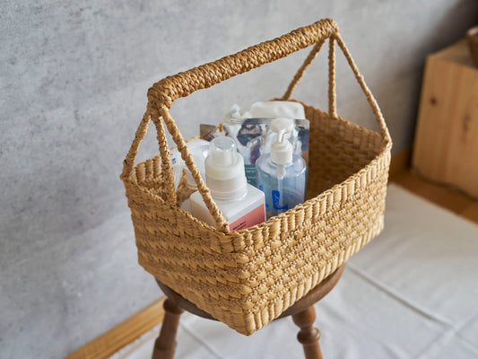 Water hyacinth square gondola basket with triple braid holding toiletries placed on a stool / 日用品を入れたウォーターヒヤシンスの三つ編み入り角ゴンドラバスケットをスツールの上に置いた様子