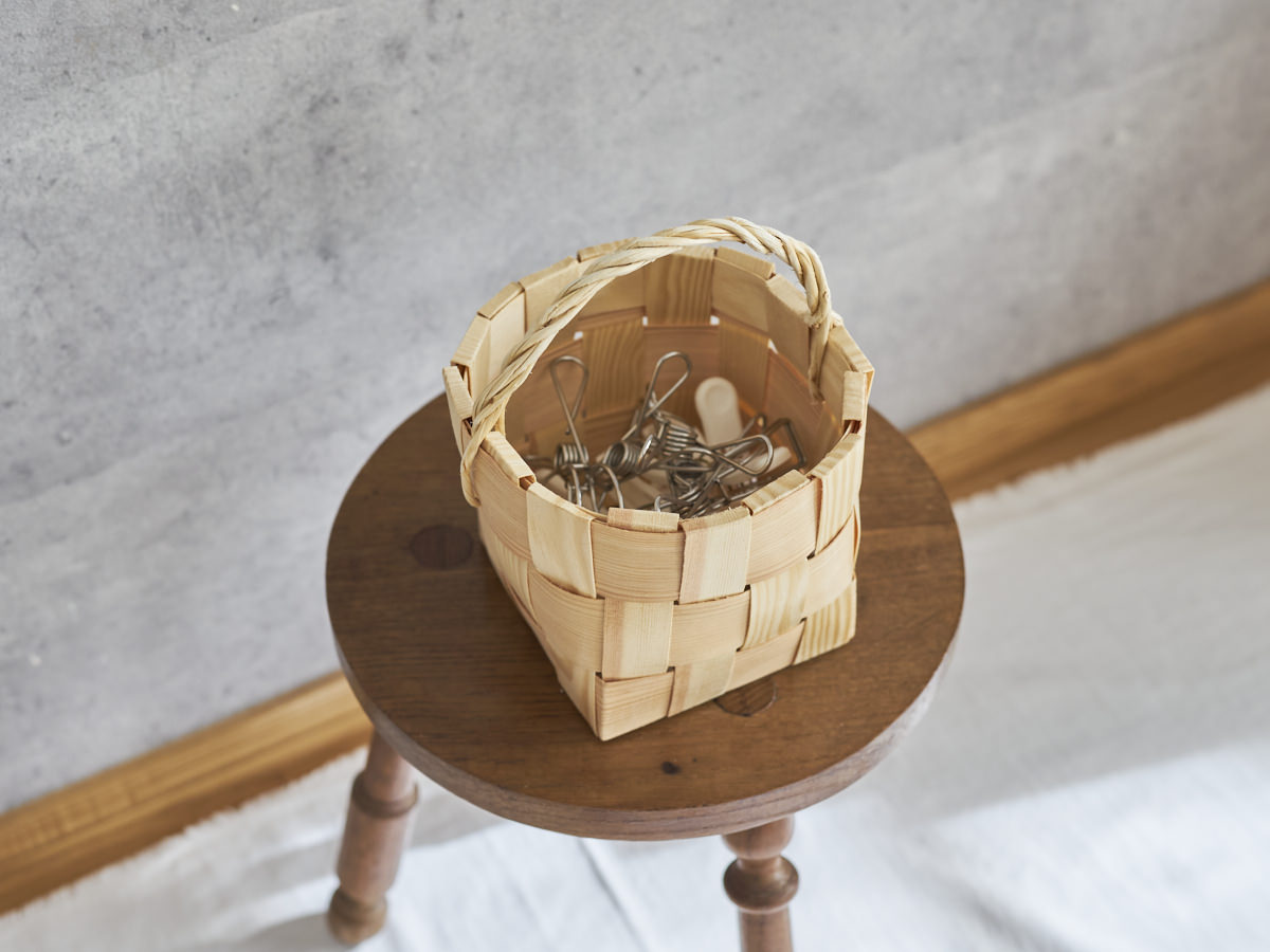 A pine pinch basket holding clothespins placed on a wooden stool / 洗濯ばさみを入れたパインのピンチバスケットを木製のスツールに置いた様子
