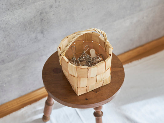 A pine pinch basket holding clothespins placed on a wooden stool / 洗濯ばさみを入れたパインのピンチバスケットを木製のスツールに置いた様子