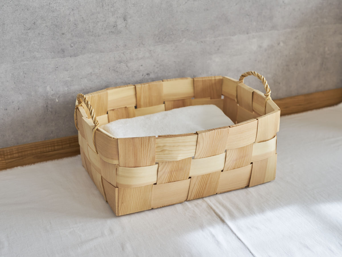 A pine laundry basket with side handles holding folded laundry / 持ち手付きのパインのランドリーバスケットに折りたたんだ洗濯物を入れた様子