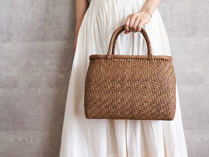 A person holding a plump grapevine basket bag with braided handles / やまぶどうの編組み手のふっくらした手提げを手に持っている様子