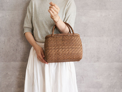 A person holding a small plump grapevine basket bag with braided handles / やまぶどうの編組み手のふっくらした小さな手提げを持っている様子